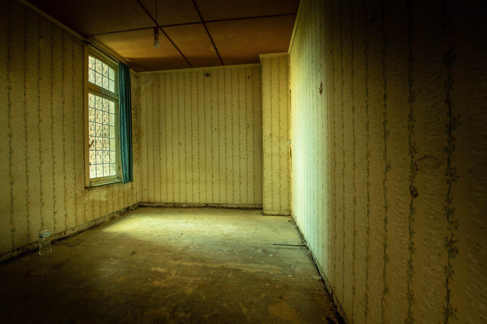 Leerer Raum mit veraltetem Tapeten, Holzfußboden und blauen Vorhängen im Fenster, schafft eine verlassene Atmosphäre