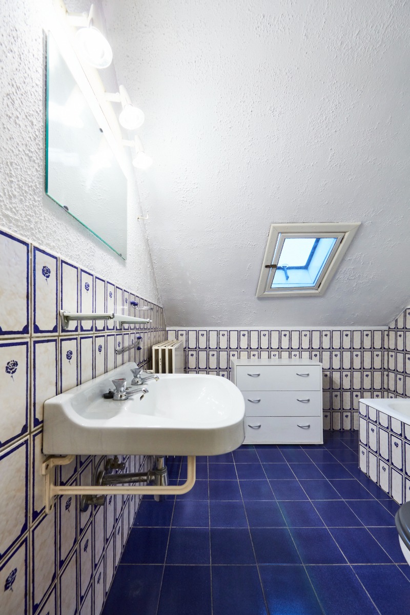 Badkamer met witte wastafel, blauwe tegels en dakraam