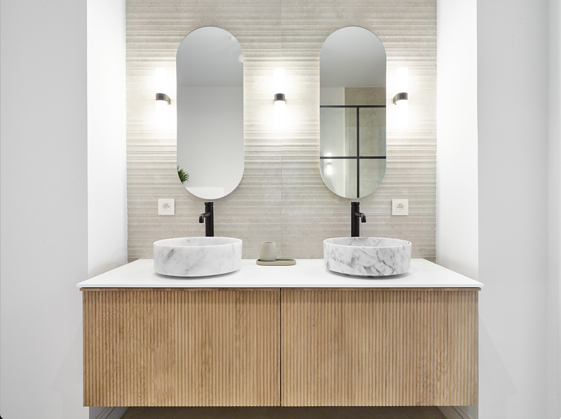 Double lavabo en marbre avec robinets chromés noirs, éclairage élégant et meuble en lin.