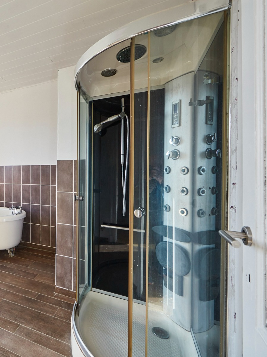 Cabine de douche avec parois en verre, plusieurs pommeaux de douche et un panneau de contrôle moderne.