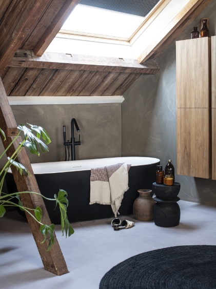 Freistehende schwarze Badewanne mit moderner schwarzer Armatur, Holzschrank und Pflanzen in einem rustikalen Badezimmer.