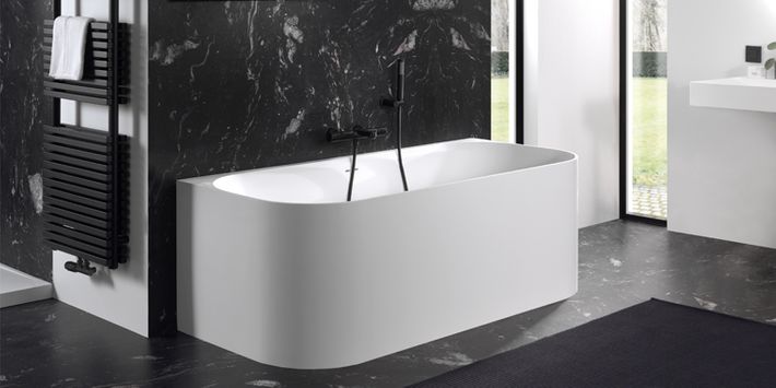 Vrijstaand bad met zwarte marmeren wand en zwarte kraan in moderne badkamer.