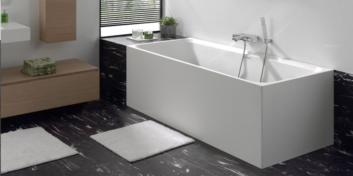 Strakke, witte vrijstaande badkuip met een moderne kraan, geplaatst op een zwart marmeren vloer.