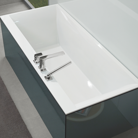 Detailansicht einer glänzend weißen Einbau-Badewanne mit integrierter Armatur in einem Designbad von x²o Badezimmer, mit klarem Kontrast zu dunklen Bodenfliesen.