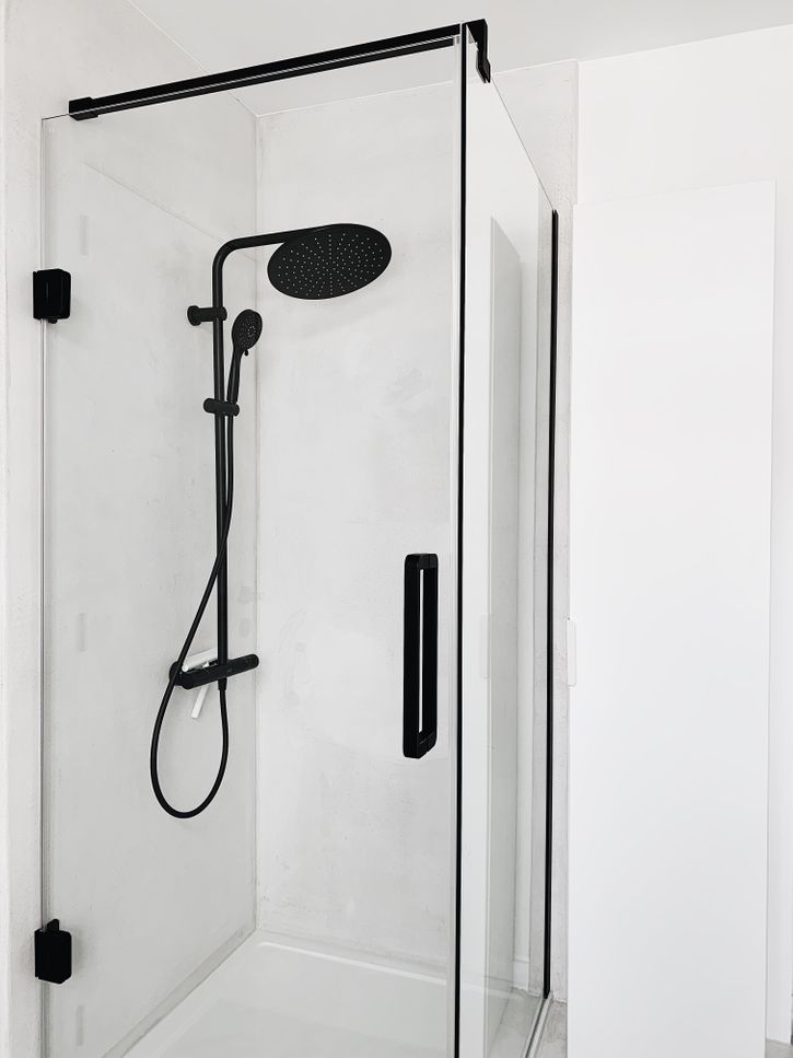 Inloopdouche met zwarte aluminium profielen en een matzwarte regendouche in een minimalistische badkamer van x²o badkamers, afgewerkt met lichte wandpanelen en een strakke witte douchevloer.