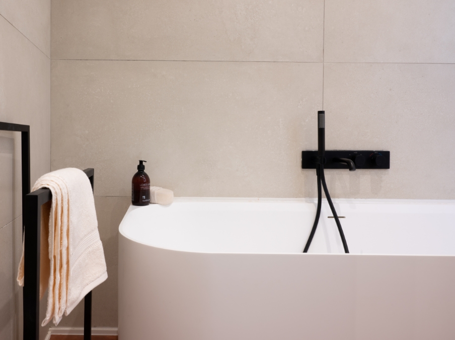 Freistehende weiße Badewanne von x²o Badezimmer mit schwarzer Badarmatur und Handbrause, kombiniert mit hellen Wandfliesen für eine elegante, zeitlose Optik.