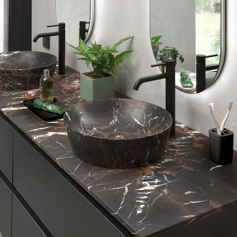 Schwarze Waschschale mit weichen Rundungen auf dunkler Platte, mit Designarmatur und Pflegeprodukten von x²o Badezimmer.