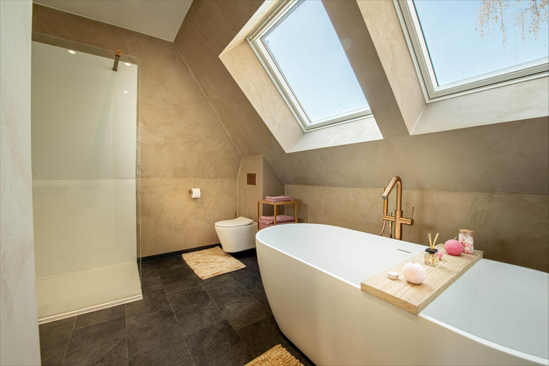 Nach der Renovierung zeigt x²o Badezimmer ein helles, modernes Badezimmer mit freistehender Badewanne, sanften Erdtönen an den Wänden, einem minimalistischen WC und viel Tageslicht durch Dachfenster.