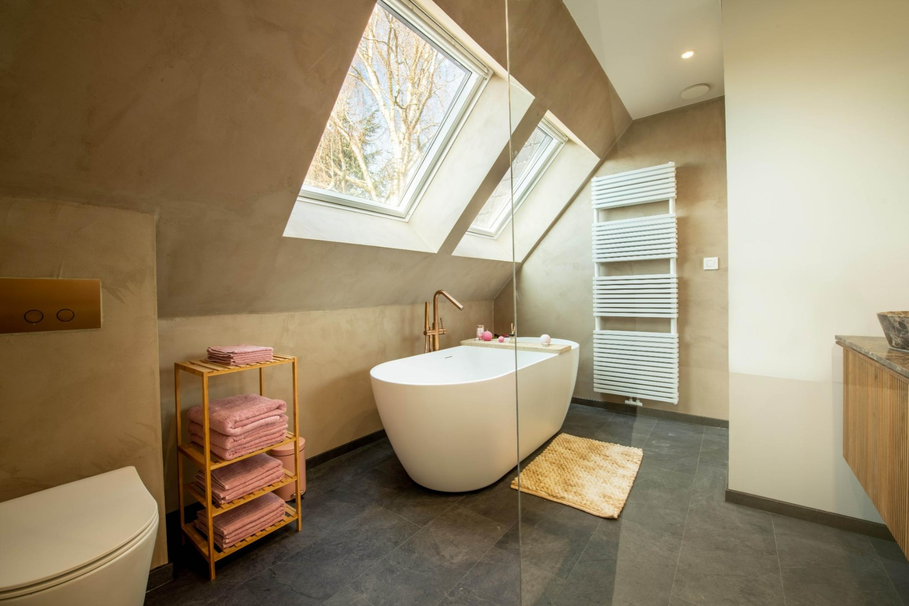 Nach dem Umbau zeigt x²o Badezimmer ein stilvolles Badezimmer mit bodengleicher Dusche und Glaswand, einem Holzbadmöbel mit zwei Natursteinwaschbecken und eleganten goldfarbenen Armaturen.