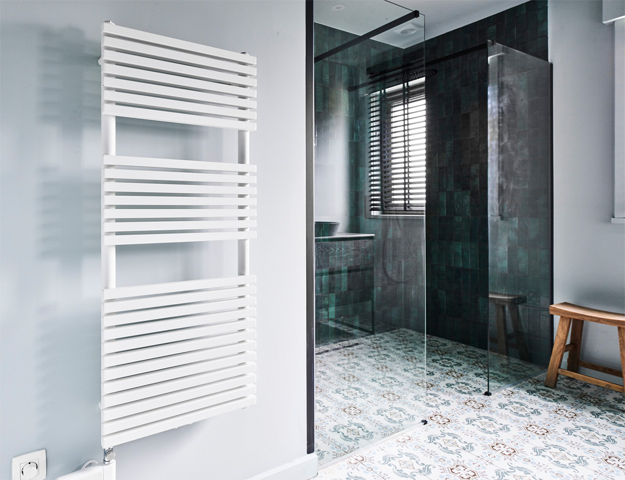 Diese Badezimmergestaltung von x²o Badezimmer zeigt eine wandhängende Toilette in schlichtem Weiß. Der Boden ist mit dekorativen Fliesen in Blau- und Graumustern versehen. An der linken Wand hängt ein weißer Designheizkörper mit horizontalen Streben vor einer hellblauen Wand, was dem Raum eine frische, moderne Ausstrahlung verleiht.