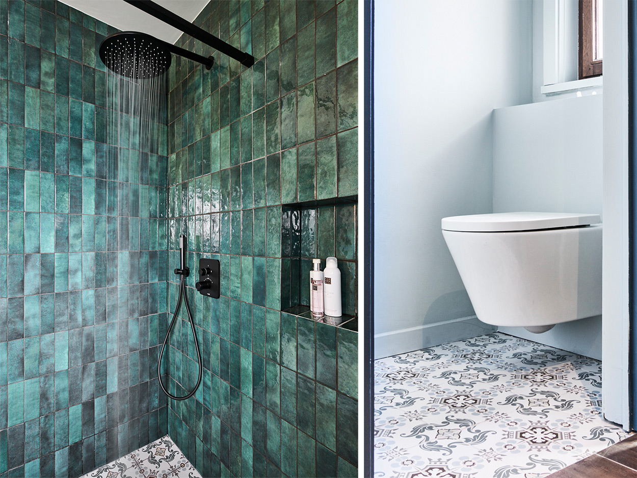 In diesem modernen Badezimmer von x²o Badezimmer ist eine bodengleiche Dusche mit glänzenden, grün-blauen Wandfliesen zu sehen, die vertikal verlegt sind. Die Dusche verfügt über eine schwarze Regendusche und eine passende Handbrause. In der Wand befindet sich eine eingelassene Nische mit Pflegeprodukten. Der Boden ist mit gemusterten Fliesen in Blau- und Grautönen gestaltet.