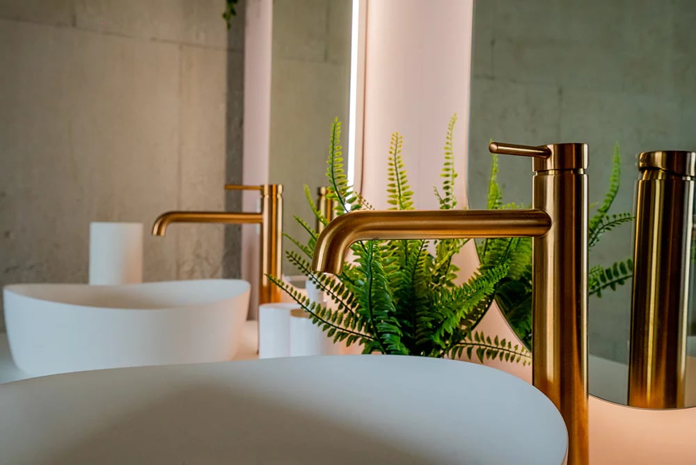 Detailaufnahme einer eleganten goldfarbenen Badarmatur neben einer freistehenden Badewanne, mit modernem Badmöbel und runden Spiegeln im Hintergrund in einer luxuriösen x²o Badezimmer Umgebung.