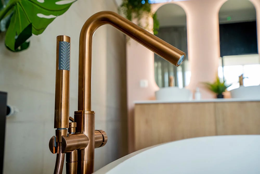 Nahaufnahme eines modernen Waschbeckens mit goldfarbener Armatur, grünen Pflanzen und sanfter Spiegelbeleuchtung, die die hochwertige Verarbeitung von x²o Badezimmer unterstreicht.