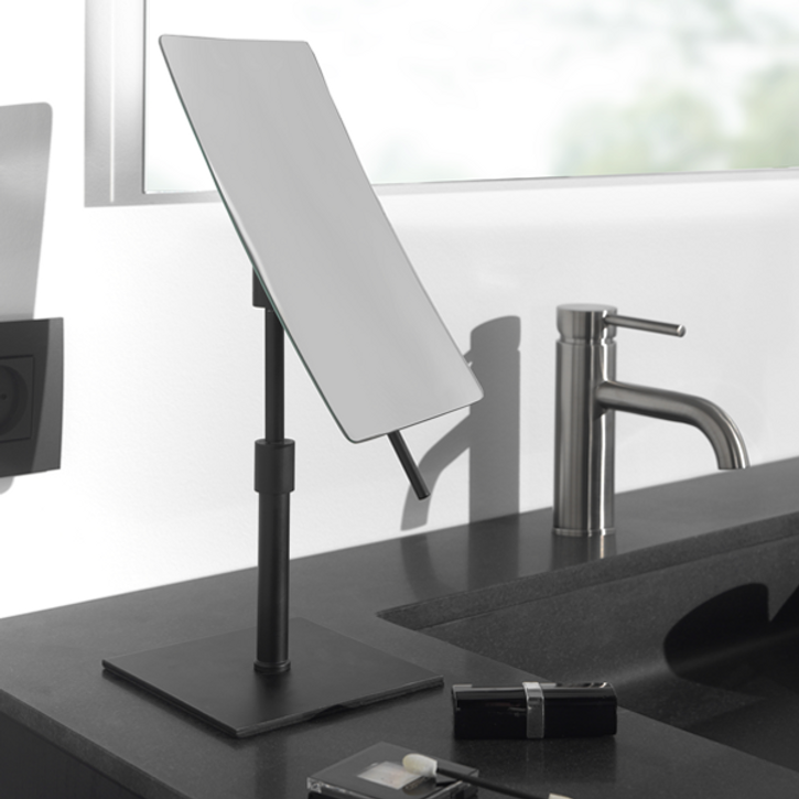 Stijlvolle badkameraccessoires rond een ronde spiegel met zachte verlichting, waaronder gouden wandhaken en decoratieve items, als cadeautip voor Moederdag bij x²o badkamers.