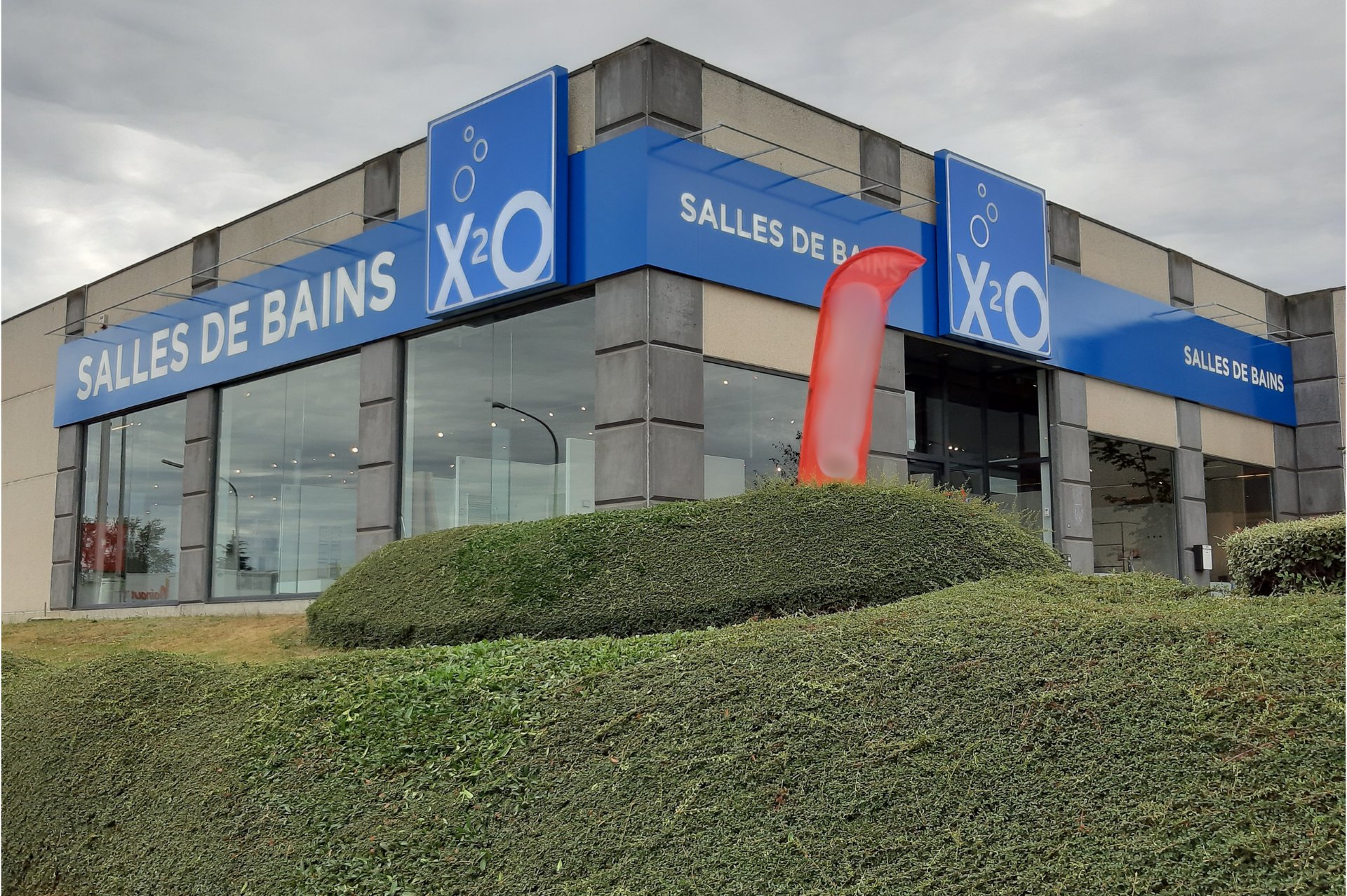 Showroom x²o salles de bains à Charleroi avec auvent bleu et façade vitrée.