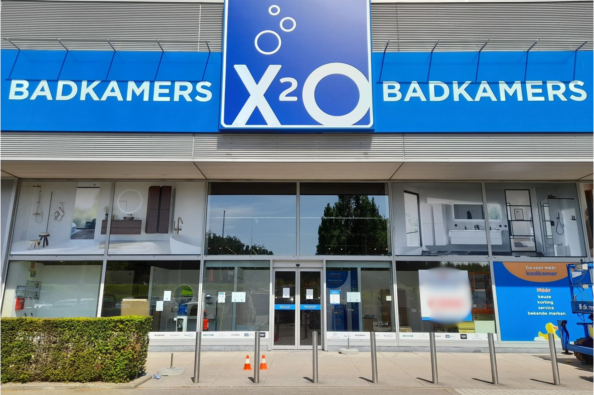 x²o badkamers showroom in Zaventem met blauwe gevel, glazen ramen en zicht op badkameropstellingen binnenin.