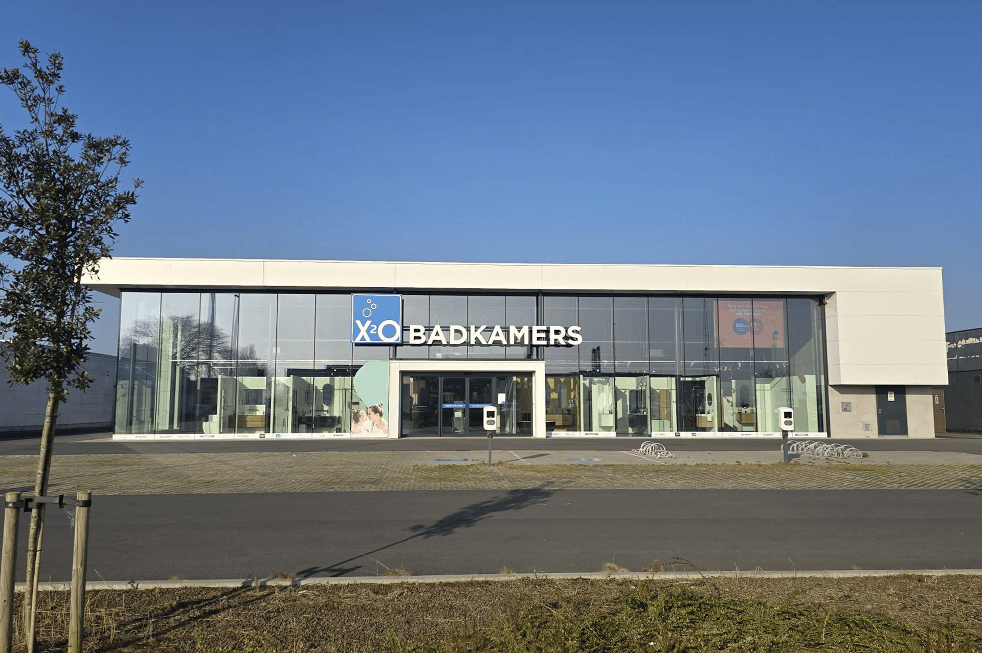 Vue frontale d’un magasin moderne X2O Salles de Bains avec une grande façade vitrée, un encadrement blanc et un ciel bleu clair en arrière-plan.
