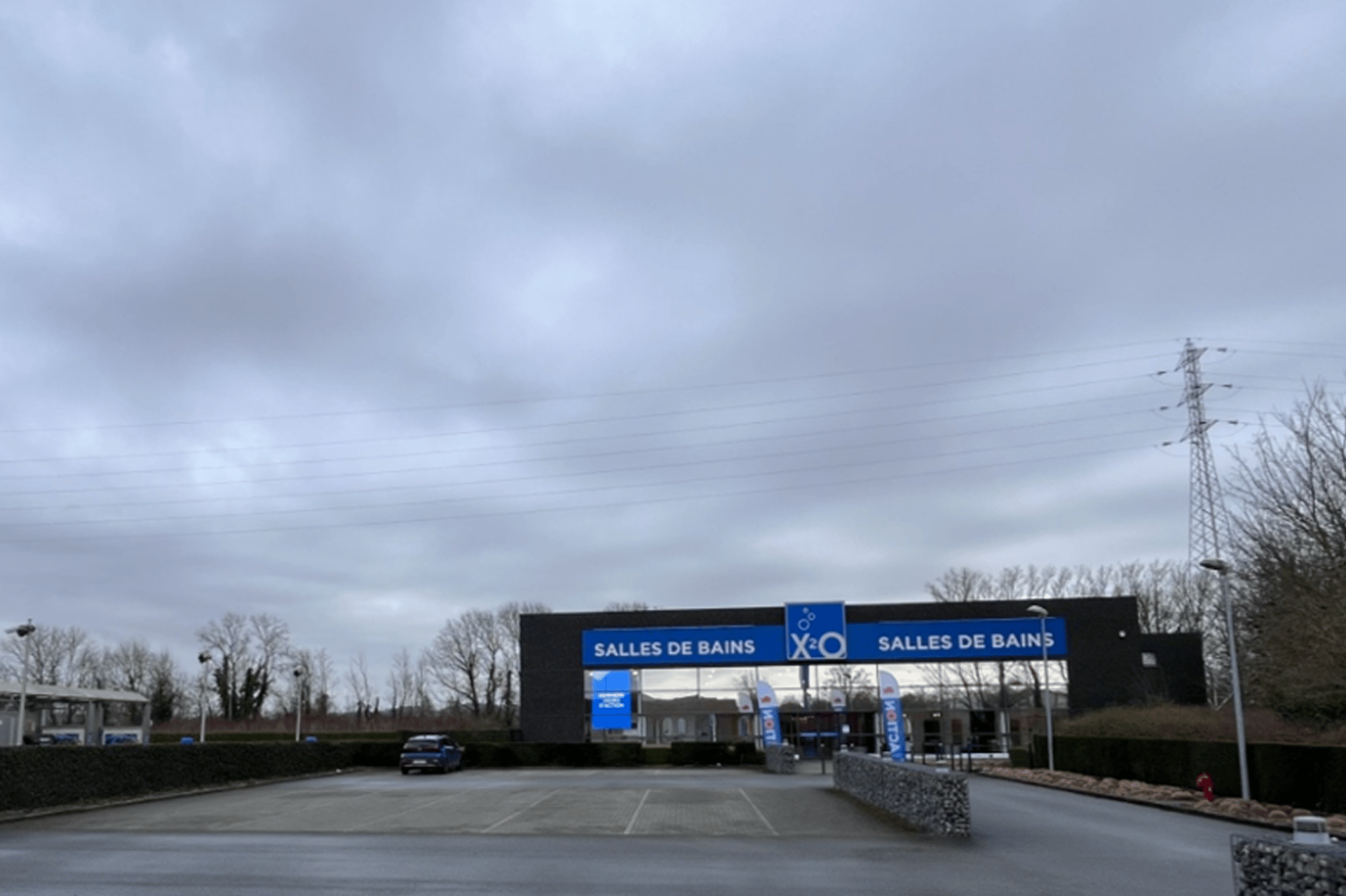 Entrée du magasin X2O Salles de Bains avec une double enseigne, un parking presque vide et un ciel couvert.