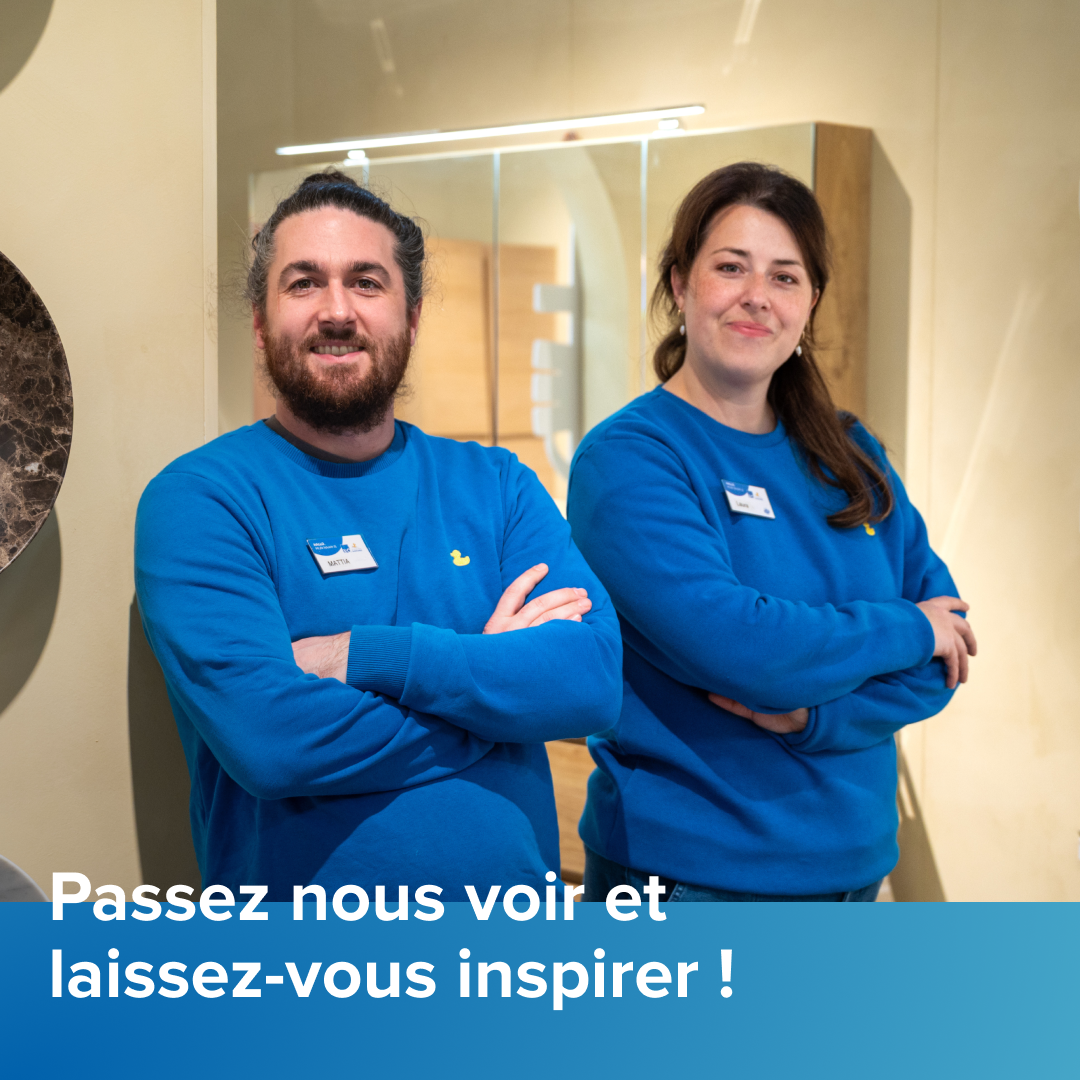 Deux collaborateurs de x²o salles de bains se tiennent les bras croisés dans un showroom de salles de bains, vêtus de pulls bleus, avec en arrière-plan une armoire miroir éclairée et du mobilier de salle de bains. Le texte « Venez nous rendre visite et laissez-vous inspirer » apparaît en bas de l’image.