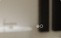 Du siehst eine unscharfe Nahaufnahme eines Badezimmerspiegels von x²o Bad mit einem dezenten Symbol für die Antibeschlag-Funktion. Im Hintergrund ist ein minimalistisches Badezimmer mit ruhigen Farben erkennbar.