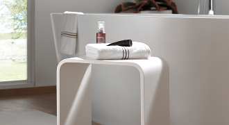 Table de salle de bains blanche avec serviette et produits de soin à côté d’une baignoire – X²O Salles de bains.