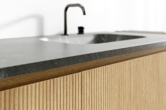 Modern wastafelmeubel met geribd hout, donker blad en zwarte kraan voor een stijlvolle en natuurlijke uitstraling.