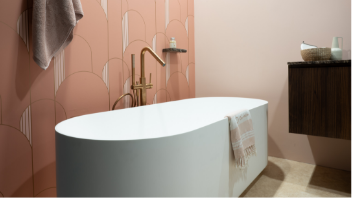 Salle de bains bien-être de x²o salles de bains avec une grande baignoire îlot Bolla placée devant un mur de carreaux verts. Une étagère murale, un tabouret en bois et un éclairage doux renforcent l’ambiance spa.