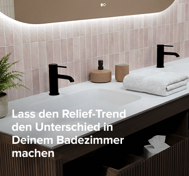 Braun geriffeltes Badezimmermöbel mit weißer Waschtischplatte, schwarzen Armaturen und beleuchtetem Spiegel vor einer Wand aus pastellrosa Fliesen.