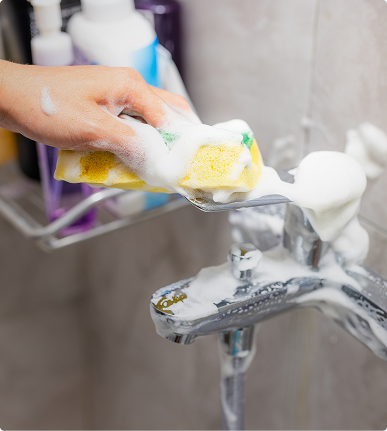 Schäumender Schwamm auf einer verchromten Duscharmatur beim Reinigen – X²O Badezimmer