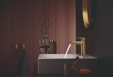 Goldener Wasserhahn über einem weißen Waschbecken in einer minimalistischen, stilvollen Umgebung.