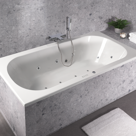 Rechteckige Einbau-Badewanne mit verchromter Badarmatur und Handbrause in einem Badezimmer von x²o Badezimmer, kombiniert mit grauen Fliesen in Marmoroptik und sanfter Beleuchtung.
