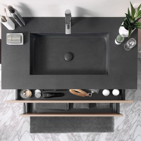 Ingebouwde zwarte wastafel gezien van bovenaf, geplaatst in een donker werkblad met kraan, accessoires en open opbergruimte, bij x²o badkamers.