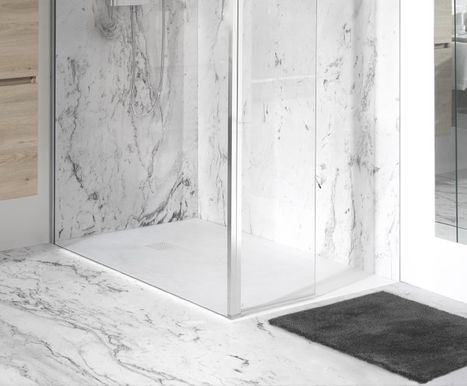 Weiße Duschwanne in einer bodengleichen Dusche mit transparenten Glaswänden, umgeben von Boden- und Wandfliesen in Marmoroptik. Vor der Dusche liegt eine dunkle Badematte. Diese elegante Lösung von x²o Badezimmer vereint Sauberkeit und Pflegekomfort.