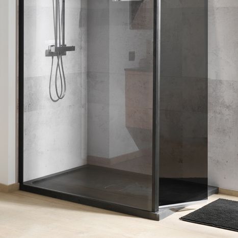 Dunkle bodengleiche Dusche mit transparenter Glaswand und schwarzer Duschwanne vor hellgrauen Wandfliesen. Die matte Duschwanne ist mit einer schwarzen Duscharmatur kombiniert. Diese moderne Duschlösung von x²o Badezimmer zeigt eine pflegeleichte und minimalistische Badgestaltung.
