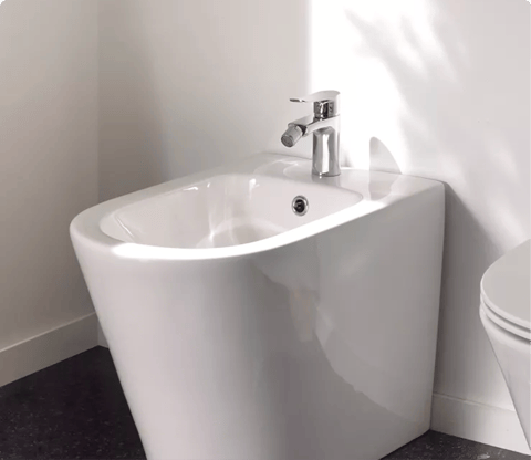 Un bidet blanc avec robinet chromé, positionné à côté d’un WC assorti sur un sol sombre. Design simple et efficace de x²o badkamers.