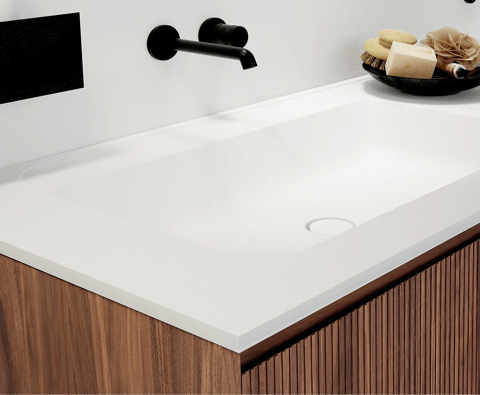 Detail van een witte ingebouwde wastafel van x²o badkamers op een houten meubel met fijne verticale ribstructuur en zwarte kraan.
