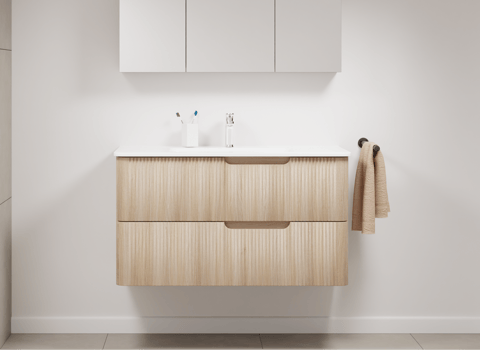 Compact badkamermeubel van x²o badkamers met afgeronde houten fronten, witte wastafel en minimalistische witte kast erboven.