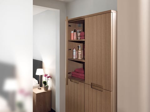 Houten badkamerkast met open deur, toont opbergplanken gevuld met handdoeken en verzorgingsproducten.