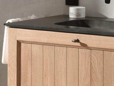 Detail van een houten wastafelmeubel met donker stenen blad, ingebouwde wastafel en klassieke ladeknop.