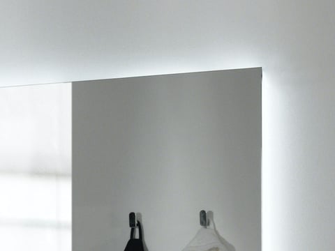 Detail van een verlichte spiegel met een strak, minimalistisch ontwerp en handdoekhaken ernaast.