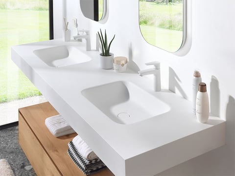 Minimalistische dubbele wastafel in wit solid surface met geïntegreerde wasbakken en moderne kranen.