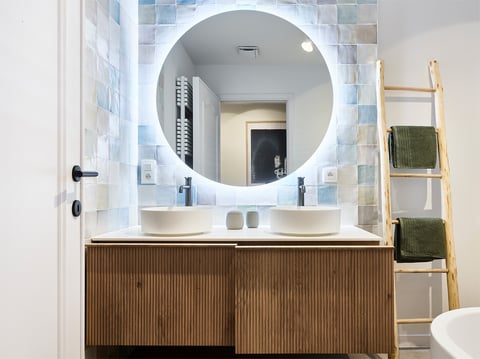 Moderne badkamer met dubbele wastafel, ronde spiegel en handdoeken op ladderrek
