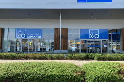 Magasin X²O salles de bains avec large entrée, façade vitrée et végétation devant le bâtiment – X²O salles de bains