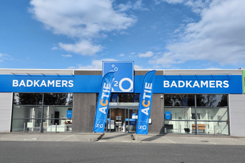 Magasin X²O salles de bains avec façade symétrique, entrée centrale et drapeaux promotionnels – X²O salles de bains