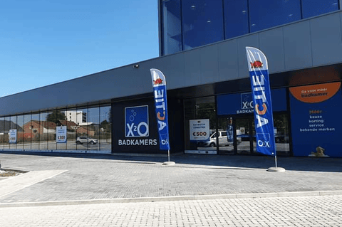 Magasin X²O salles de bains avec façade vitrée, drapeaux promotionnels et entrée spacieuse côté rue – X²O salles de bains