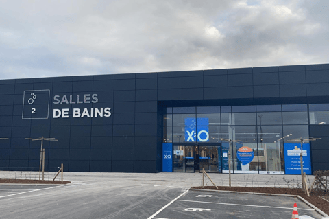 Magasin X²O salles de bains avec façade sombre moderne, entrée vitrée et parking devant le bâtiment – X²O salles de bains