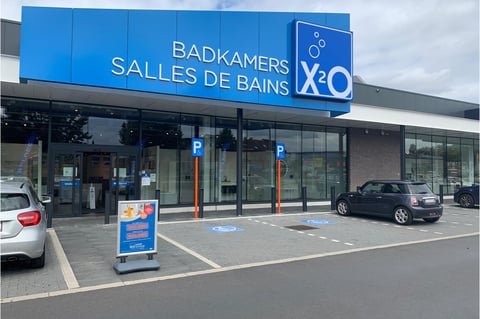 Showroom x²o salles de bains à Drogenbos avec enseigne bleue et façade moderne en verre.