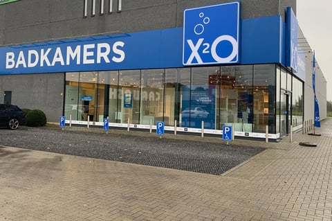 x²o badkamers showroom in Geel met blauwe gevel, grote ramen en parking voor de ingang.