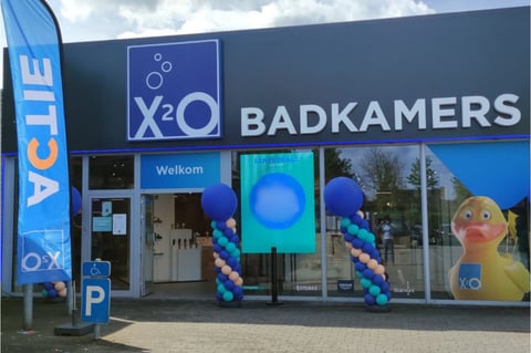 Magasin x²o salles de bains à Tielt-Winge avec drapeaux “ACTIE”, décorations de ballons et promotions visibles.