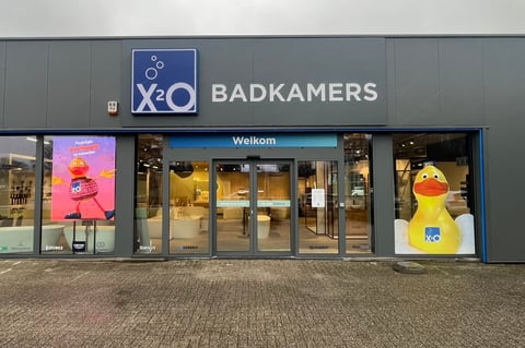 Façade du showroom x²o salles de bains à Turnhout avec enseigne bleue et installations visibles à l’intérieur.